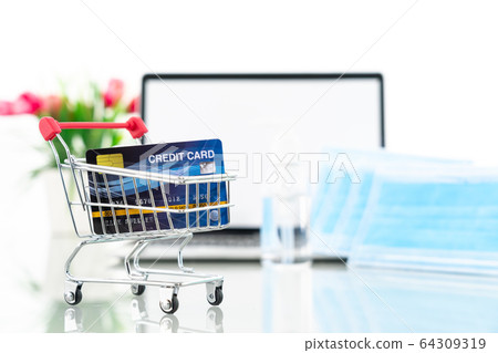 Credit card in shopping cart front of laptop 64309319