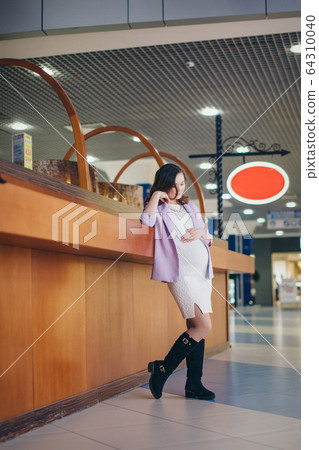 a pregnant woman is stroking her stomach. a girl waiting for a child walks in a shopping center. The concept of a healthy lifestyle , IVF, fashion for pregnant women, children 64310040