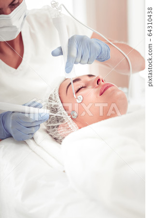 Cosmetologist wearing white uniform doing face cleansing for woman 64310438