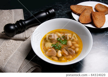 Bean soup in white plate, several toast on white 64314020