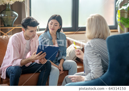 Dark-haired tall man and his girlfriend reading something and looking attentive Dark-haired tall man and his girlfriend reading something and looking attentive 64314150