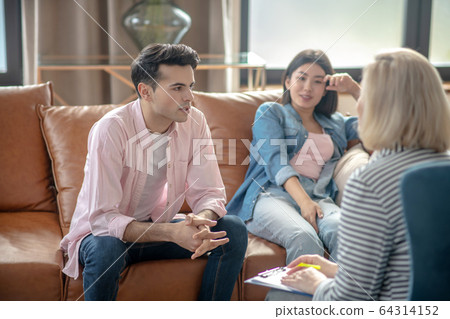 Dark-haired tall man sitting next to his girlfriend and listening to the psychologist Dark-haired tall man sitting next to his girlfriend and listening to the psychologist 64314152