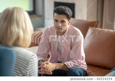 Dark-haired tall man sitting on the sofa and looking upset Dark-haired tall man sitting on the sofa and looking upset 64314154