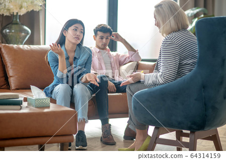 Dark-haired tall man sitting next to his girlfriend and looking indifferent Dark-haired tall man sitting next to his girlfriend and looking indifferent 64314159
