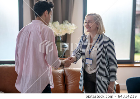 Blond psychologist greeting her young male patient in her office and smiling 64314219