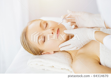 Beautician doctor doing beauty procedure with syringe to caucasian female face in synny room. Cosmetic medicine and surgery, beauty injections concept 64314670