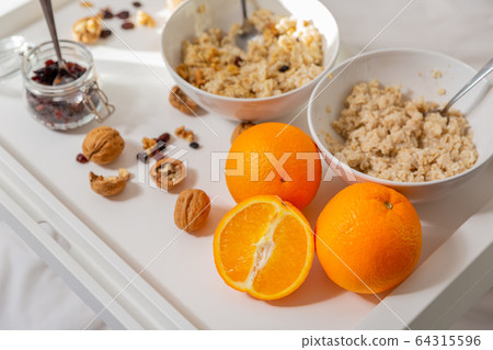 Happy mom and daughter have healthy breakfast on bed in a light bedroom on a sunny morning. Orange Happy mom and daughter have healthy breakfast on bed in a light bedroom on a sunny morning. Orange 64315596