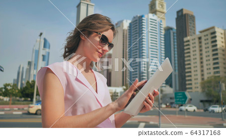 A girl works on a tablet against the background of skyscrapers of a metropolis. A girl works on a tablet against the background of skyscrapers of a metropolis. 64317168