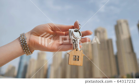 The concept of buying an apartment. Girl holds the keys to a new house against the backdrop of skyscrapers in the city. 64317232