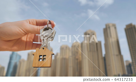 Real estate purchase concept. The girl holds the keys to a new house on the background of a Dubai skyscraper. Real estate purchase concept. The girl holds the keys to a new house on the background of a Dubai skyscraper. 64317233