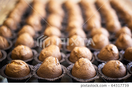 Lots of delicious fresh chocolate muffins muffins on a tray, background, copy space, dessert, manufacturing 64317739
