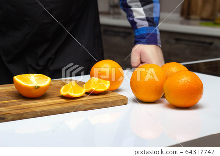 A man cuts with a knife in the kitchen juicy and fresh oranges. The concept of healthy eating and making orange juice, copy space 64317742