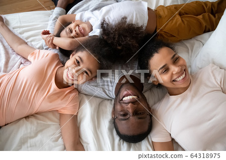 Happy african american parents with little children lying on bed. Happy african american parents with little children lying on bed. 64318975