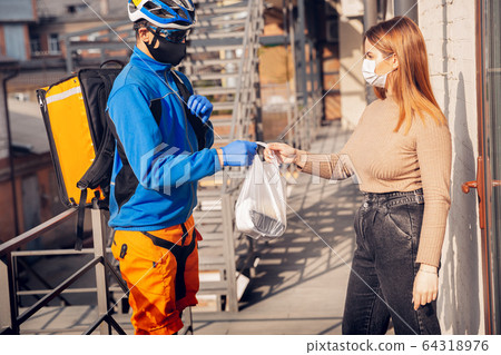 Contacless delivery service during quarantine. Man delivers food and shopping bags during isolation 64318976
