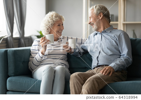 Happy mature couple drinking tea in cozy living room Happy mature couple drinking tea in cozy living room 64318994