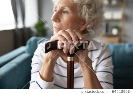 Close up thoughtful older woman holding hands on wooden cane Close up thoughtful older woman holding hands on wooden cane 64318996