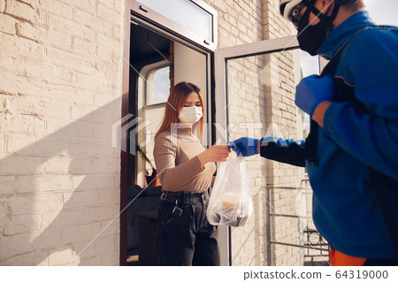 Contacless delivery service during quarantine. Man delivers food and shopping bags during isolation 64319000