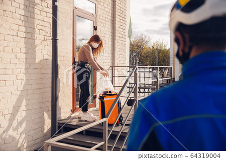 Contacless delivery service during quarantine. Man delivers food and shopping bags during isolation 64319004