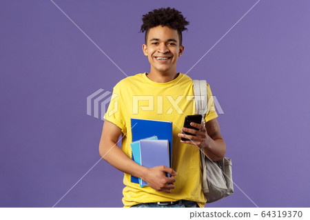 Back to school, university concept. Portrait of cheerful young handsome male student wearing backpack on shoulder, hold notebooks and studying books, texting friend mobile phone 64319370
