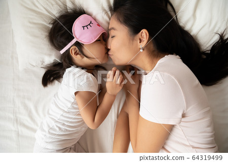 Asian mom kisses little daughter before bedtime sleeping above view 64319499