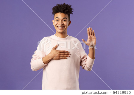 Portrait of young happy, joyful hispanic man making honest statement, promise to tell only truth, hold one hand on heart and another raised, smiling sincere, standing purple background 64319930