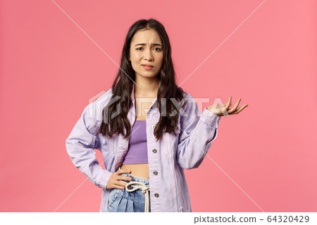 So what, I dont care. Portrait of skeptical, unimpressed and careless stylish girl, smirk unbothered shrugging and raise hand in dismay, listen to nonsense, standing pink background 64320429