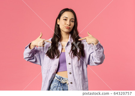 Portrait of cool and sassy stylish young woman pointing at herself with confident face, smirk and look camera as what you waiting for, pick me, bragging, being boastful, pink background 64320757
