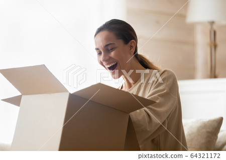 Excited young woman unpacking huge carton box. Excited young woman unpacking huge carton box. 64321172