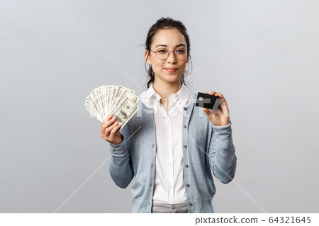 Business, finance and investment concept. Confident good-looking asian girl in glasses, female employee invest money, make good purchase or deposit, show cash dollars and credit card smile satisfied 64321645