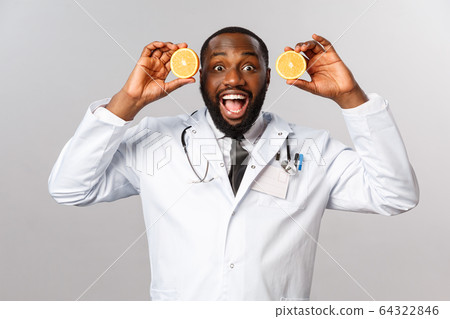 Healthcare, healthy diet and disease concept. Excited handsome african-american doctor in white coat, showing pieces of oranges and smiling amused, advice eat more food consist vitamin c, fruits Healthcare, healthy diet and disease concept. Excited handsome african-american doctor in white coat, showing pieces of oranges and smiling amused, advice eat more food consist vitamin c, fruits 64322846