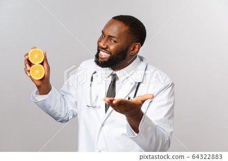 Healthcare, healthy diet and disease concept. Handsome cheeky african-american doctor pointing at patient, explain ways of staying safe and eating more vitamins, hold oranges and smiling 64322883