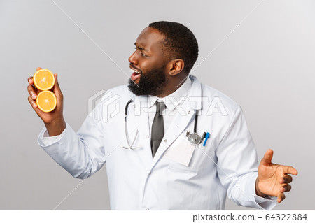 Healthcare, healthy diet and disease concept. Excited handsome african-american doctor, physician explaining pros of fruits and vegetables, look at oranges, prescribe vitamin diet, grey background 64322884