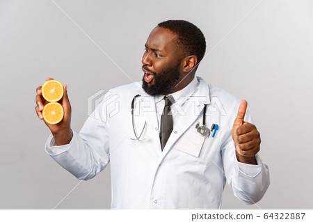 Healthcare, healthy diet and disease concept. Excited happy african-american male doctor, physician fascinated with how many vitamins orange consist of, show thumb-up in approval, recommend diet 64322887