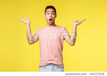 Vacation, summer and people concept. Portrait of surprised handsome, startled asian man gasping, raise hands sideways in amazement and awe, react to wonderful astonishing news, yellow background 64327636