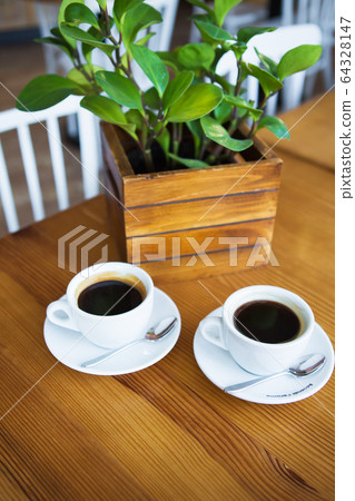 Two mugs of coffee on a wooden table, green pot. Two mugs of coffee on a wooden table, green pot. 64328147