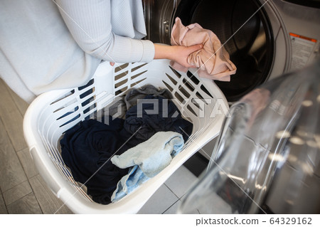 Pretty young woman putting, getting some dirty clothes into a washing machine in a laundry, laundry cleaning 64329162