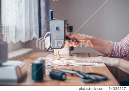 Woman sewing medical masks on sewing machine during coronavirus pandemic, protection against covid-2019, homemade sewing Woman sewing medical masks on sewing machine during coronavirus pandemic, protection against covid-2019, homemade sewing 64329237