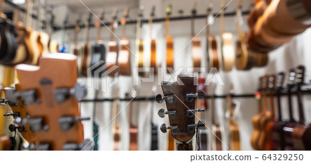 Close up of classic guitar drapped in a row in a huge musical shop, instrument shop, instrument concept Close up of classic guitar drapped in a row in a huge musical shop, instrument shop, instrument concept 64329250