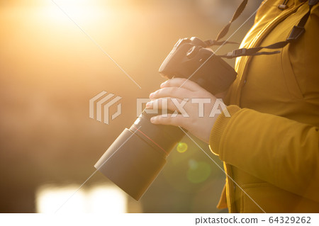 Young woman photographer with professional camer in hand during sunset 64329262