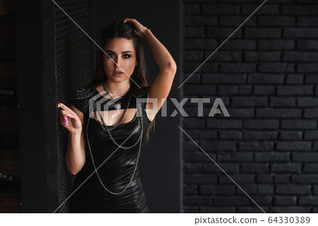 Urban stylish girl in sexual leather dress near metal grid. 64330389