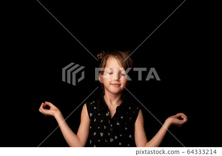 A girl of 6 years on a black background.Meditation and calm, in quarantine and distance learning. 64333214