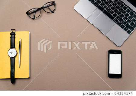 Laptop, smart phone, glasses and watch on brown office desk. 64334174
