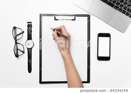 A woman's hand holds a pen and writes on a clean sheet of paper. 64334249