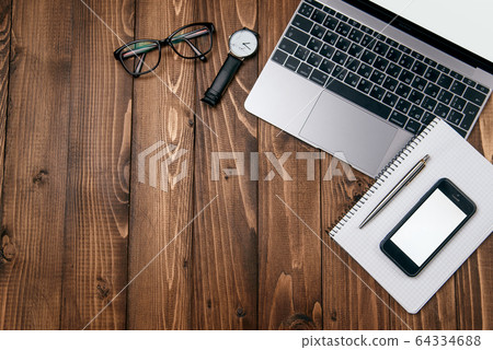 Top view photo of wooden office desk with laptop, eyeglasses, watch, smartphone and notebook with copy space background. 64334688