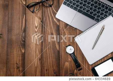Top view photo of wooden office desk with laptop, eyeglasses, watch, smartphone and notebook with copy space background. 64334689