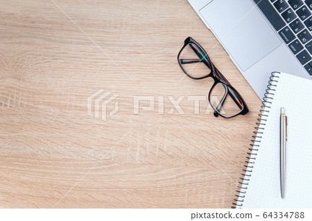 Flat lay photo of wooden office desk with laptop, eyeglasses, pen and notebook with copy space background. 64334788