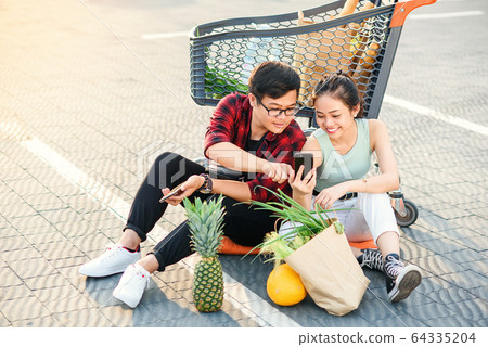 Attractive vietnamese boy and beauiful girl sitting on the parking near shopping mall and uses their smartphones. Attractive vietnamese boy and beauiful girl sitting on the parking near shopping mall and uses their smartphones. 64335204