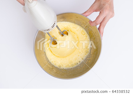 Making sweets at home, sponge dough making process Mixing eggs and sugar with a hand mixer, overhead view 64338532