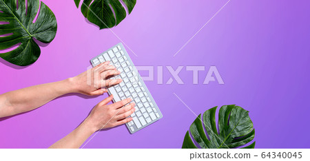 Person using a computer keyboard with tropical leaves Person using a computer keyboard with tropical leaves 64340045