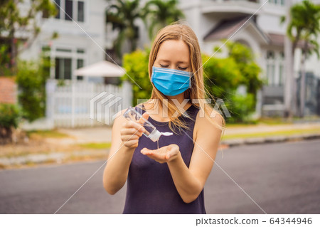 Woman in a small town in a medical mask uses a sanitizer because of a coronovirus epidemic Woman in a small town in a medical mask uses a sanitizer because of a coronovirus epidemic 64344946